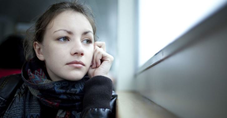 Young girl looking out the window alone
