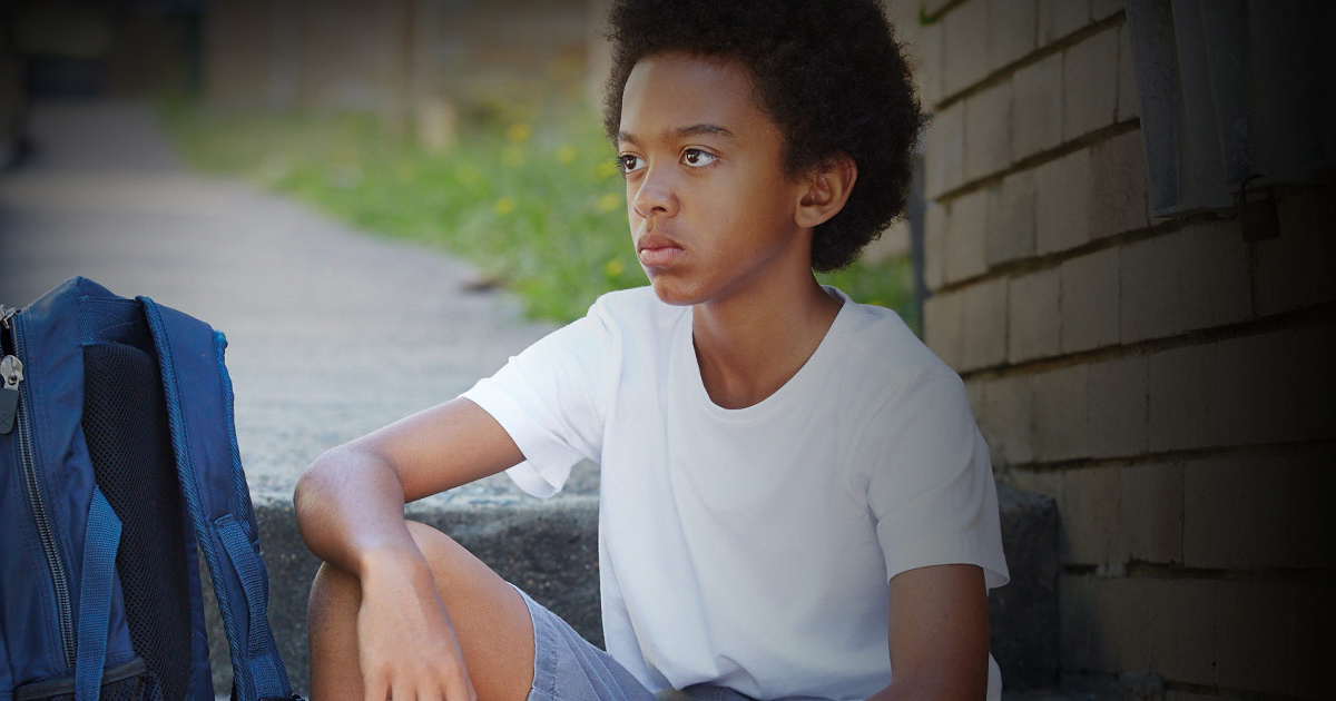 Young boy sitting on steps with school bag