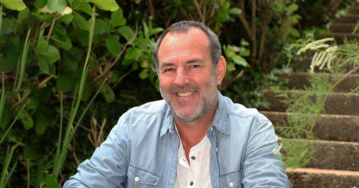 A middle aged man sitting in the garden smiling at the camera